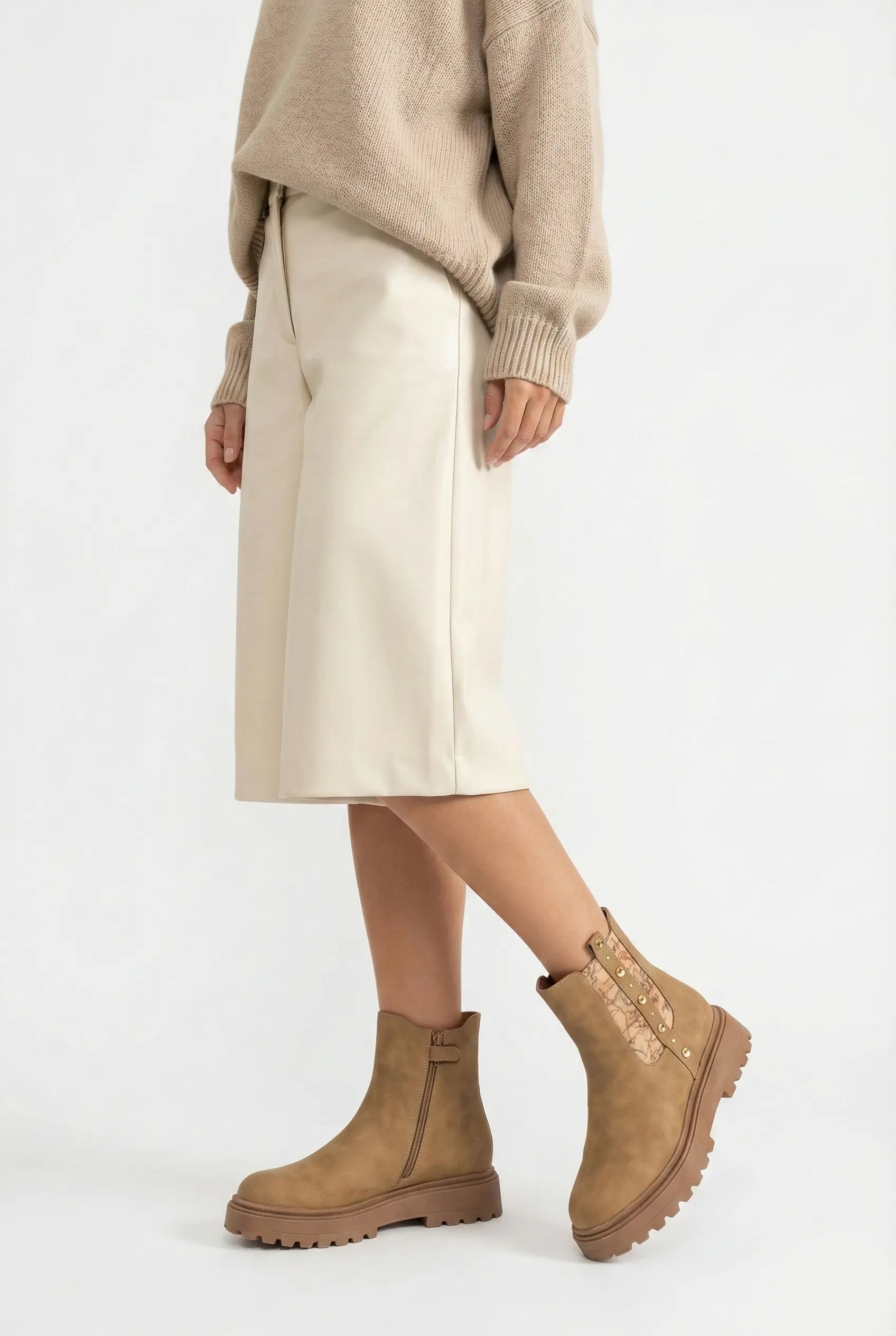 Person wearing a beige sweater, cream skirt, and brown ankle boots on a white background