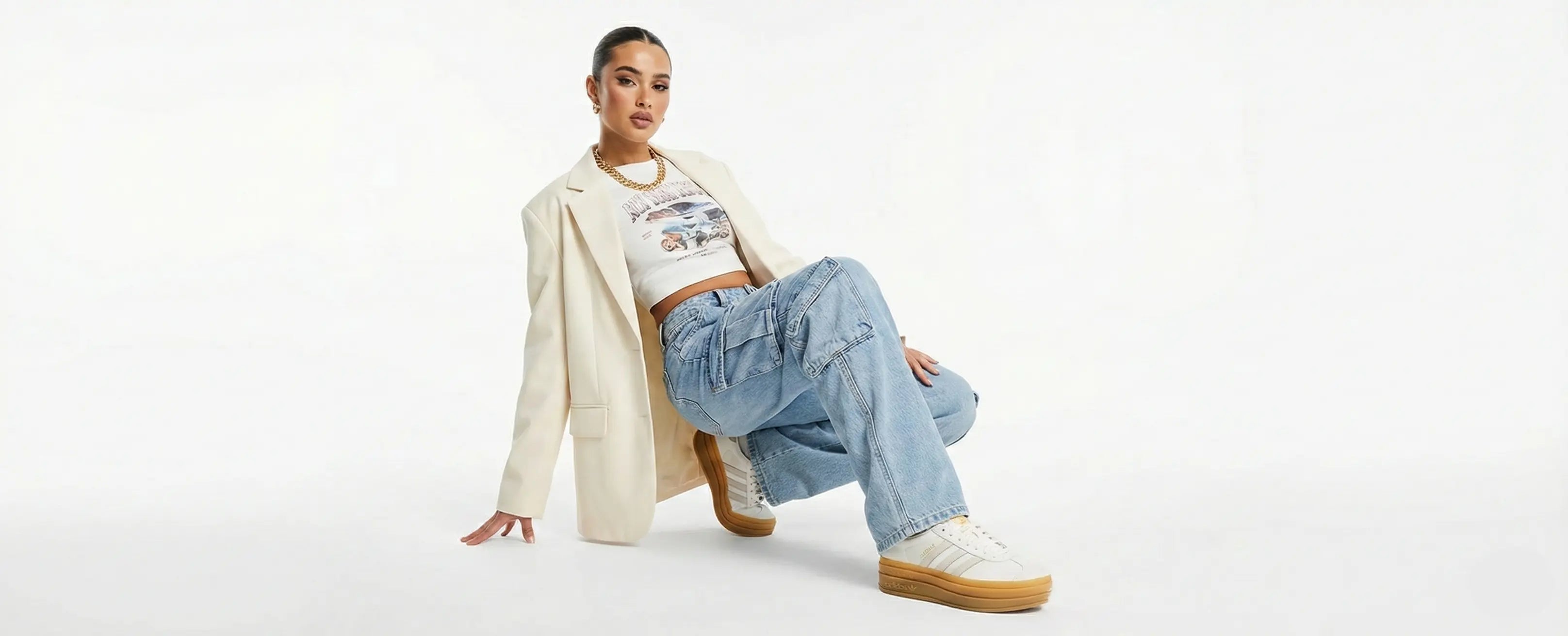 Person wearing a beige coat and blue jeans sitting on a white background