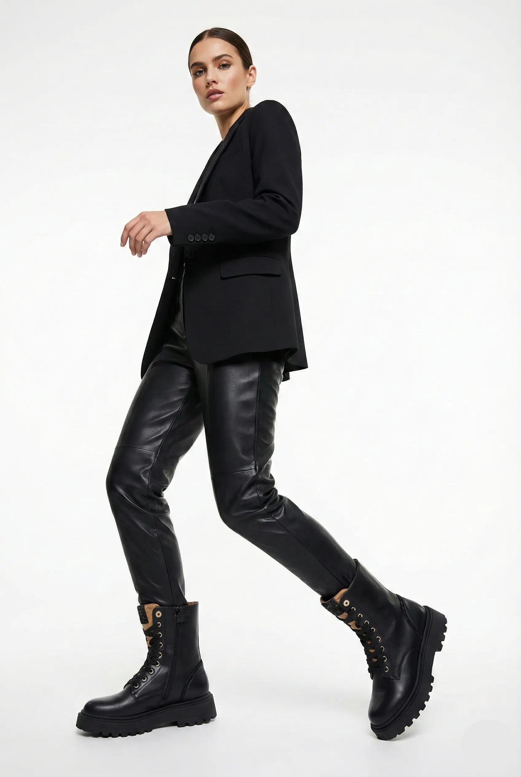 Person wearing a black outfit with leather pants and boots on a white background