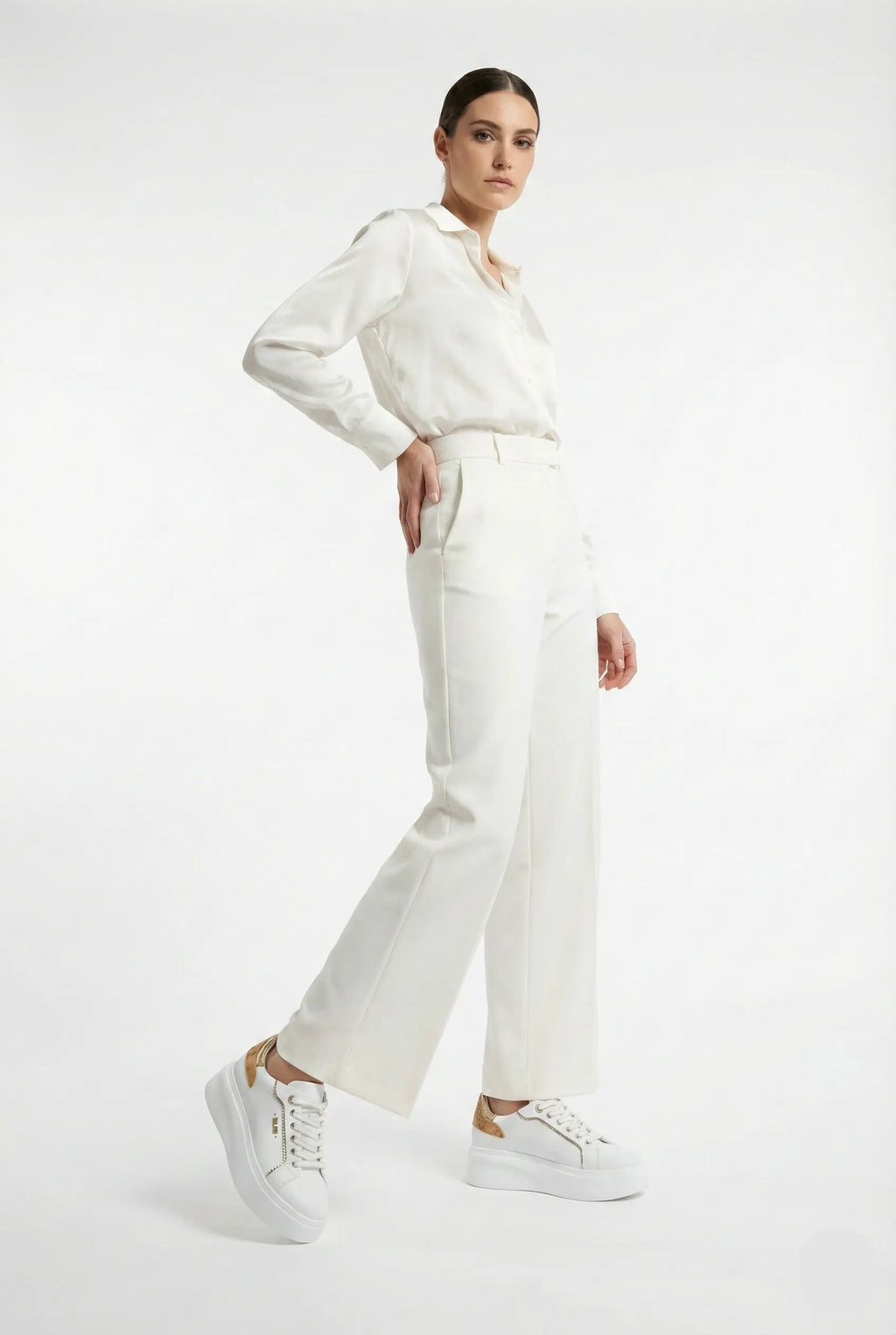 Person wearing a white blouse and pants with white sneakers on a white background