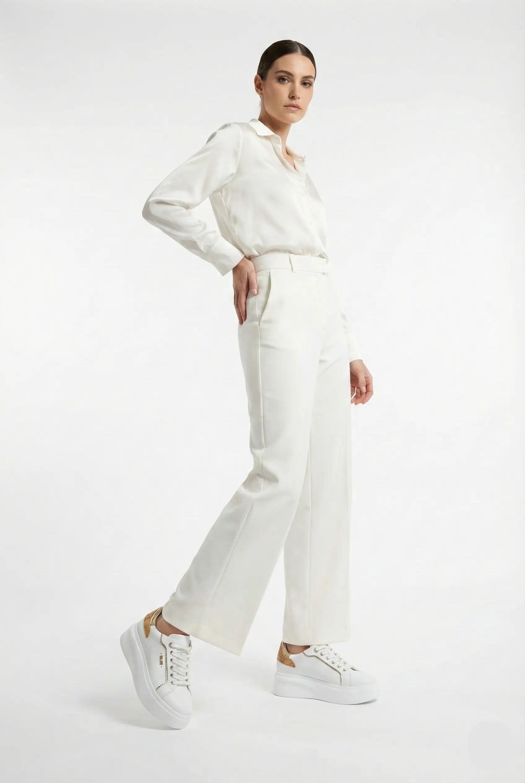 Person wearing a white blouse and pants with white sneakers on a white background