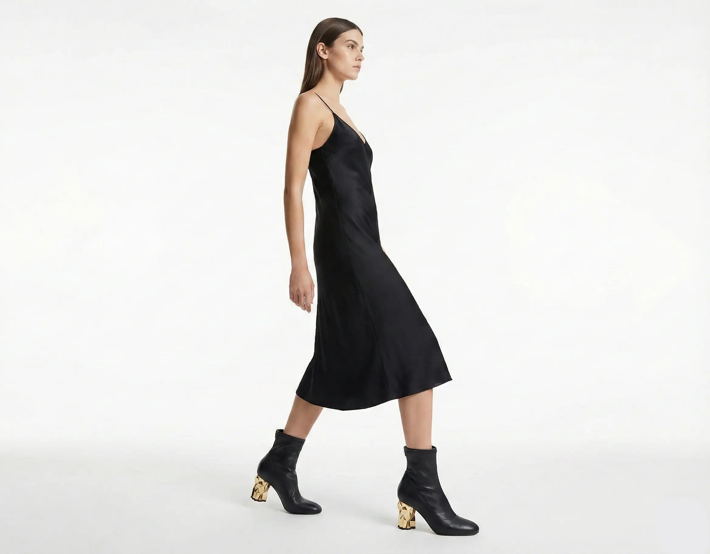 Woman wearing a black slip dress and black boots on a white background