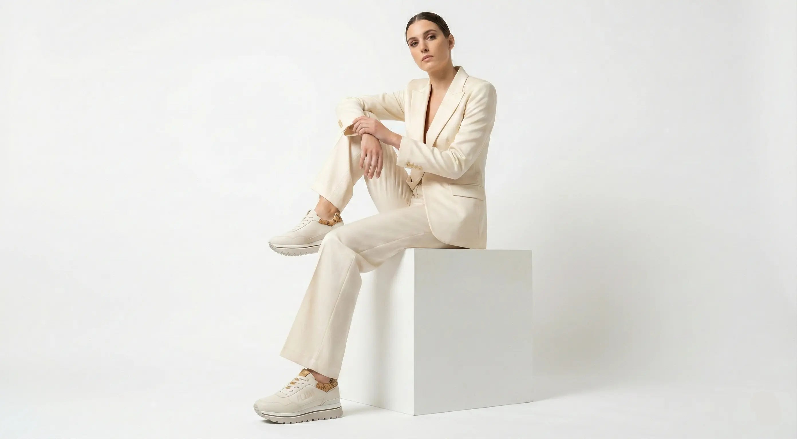 Woman in a white suit sitting on a white block against a white background