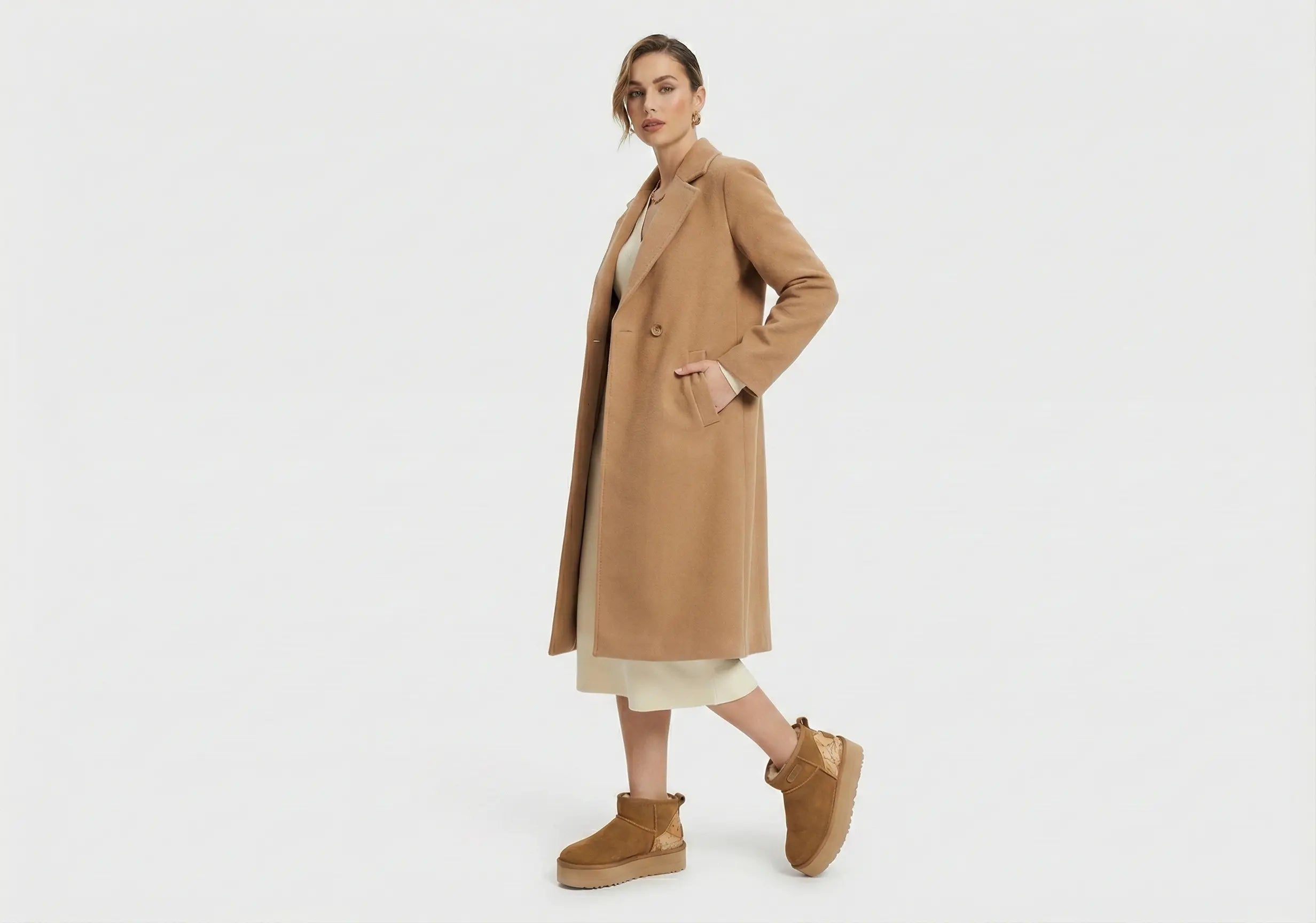 Woman wearing a tan coat and brown boots on a white background