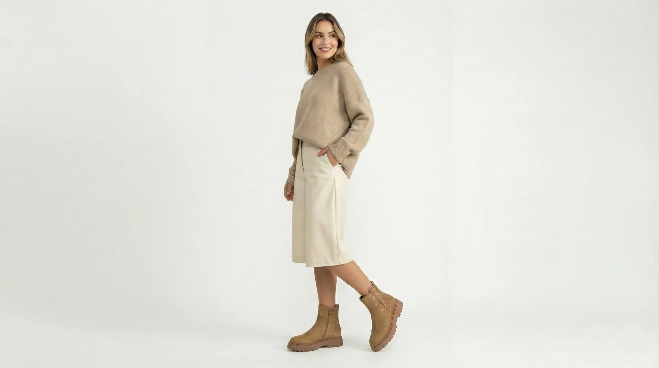 Woman wearing a beige sweater and skirt with brown boots on a white background