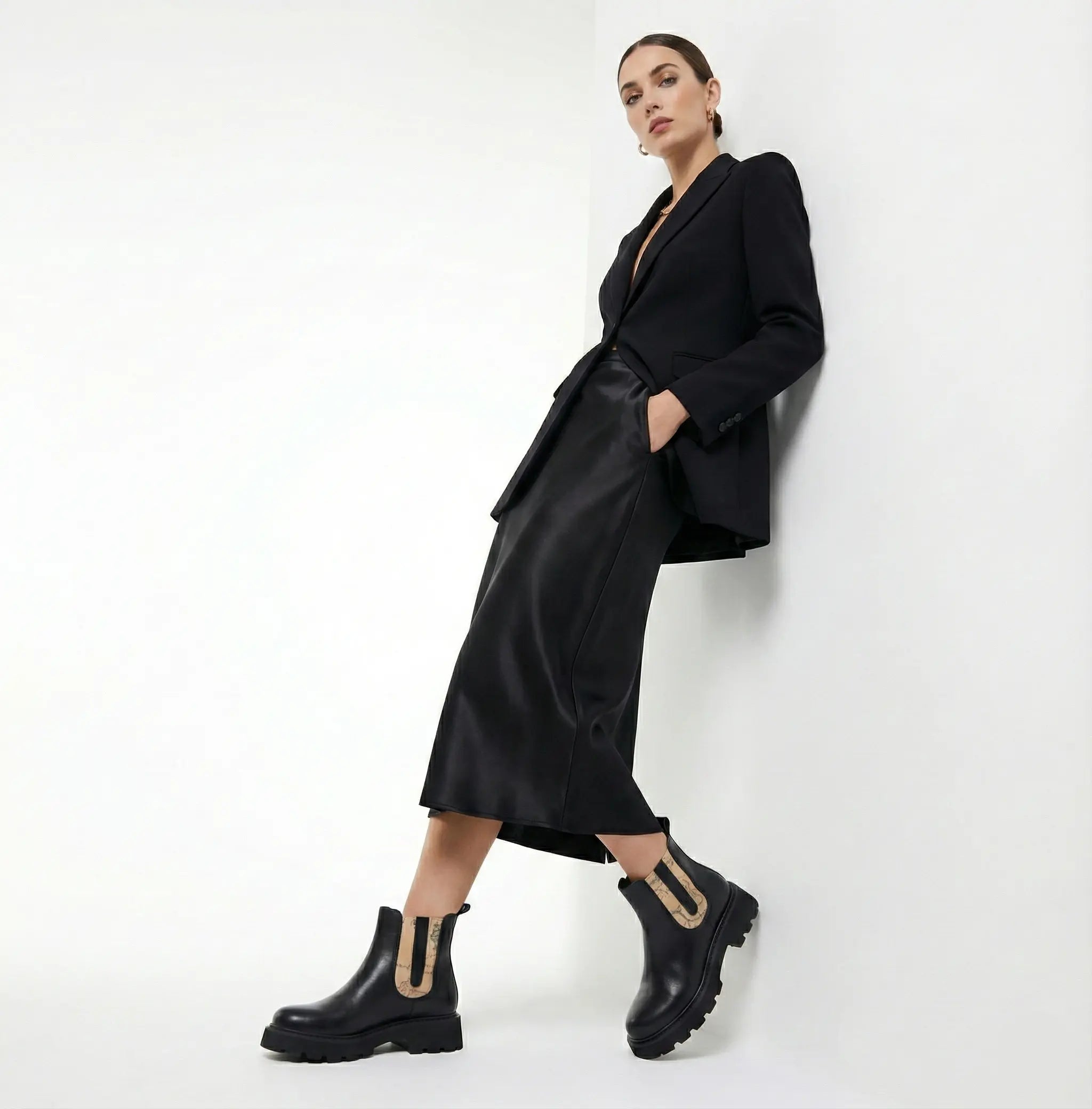 Woman wearing a black outfit with a coat and boots against a white background