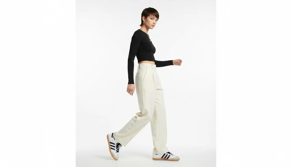 Person wearing a black top and white pants with Adidas shoes on a white background