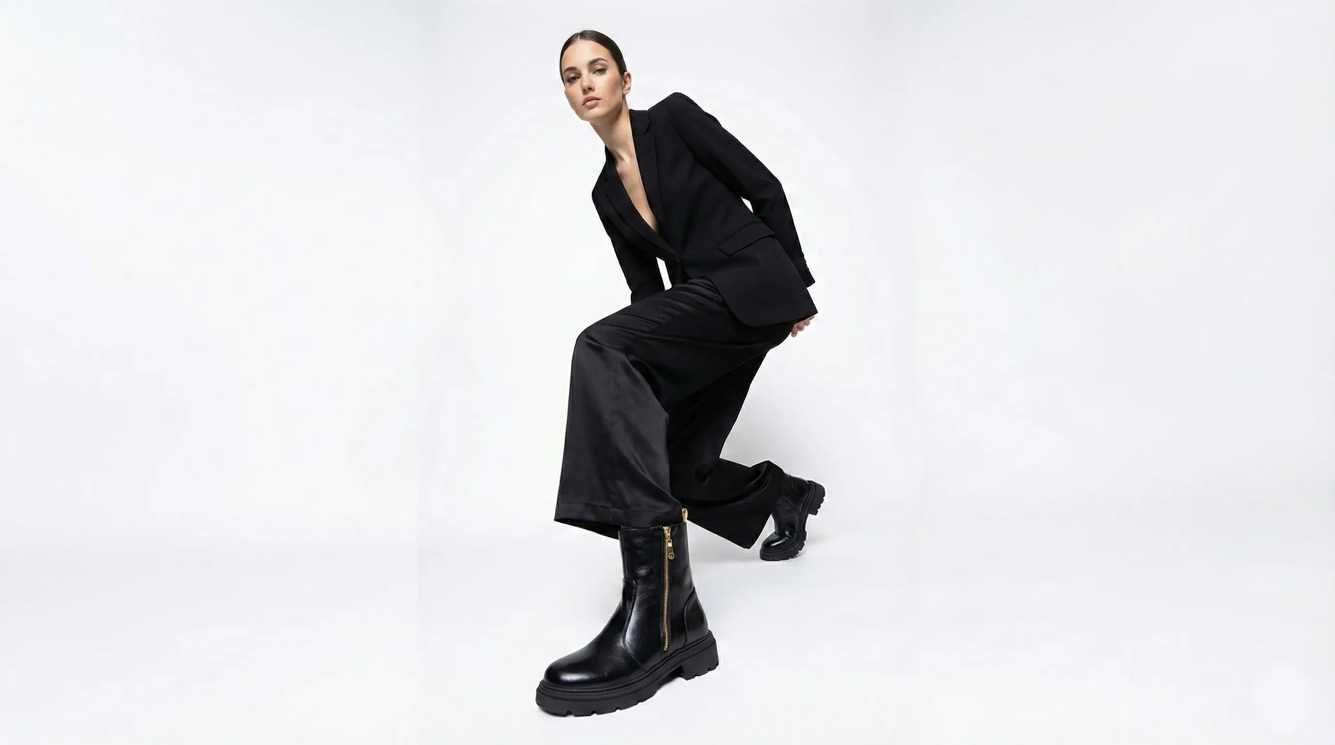 Person wearing a black suit and boots on a white background