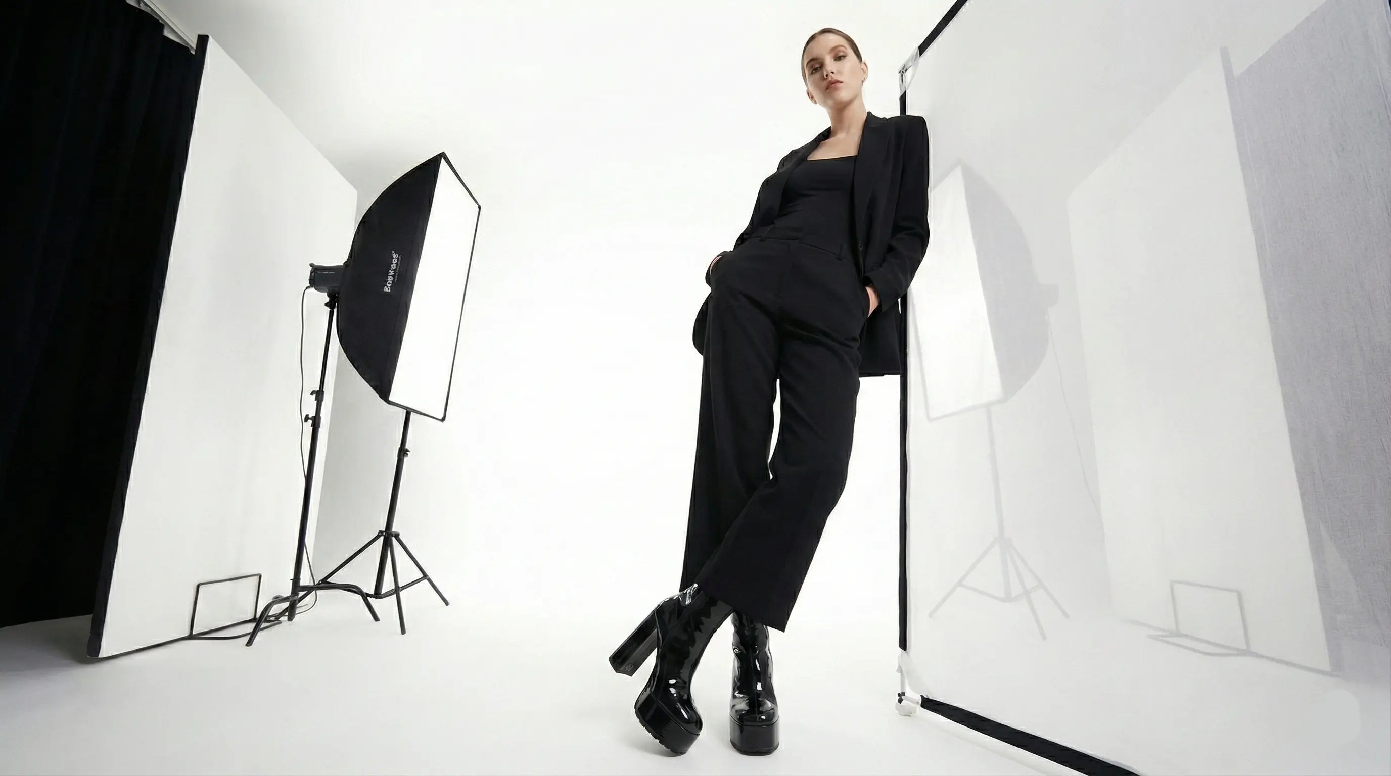Person in a black outfit sitting in a photo studio with lighting equipment.