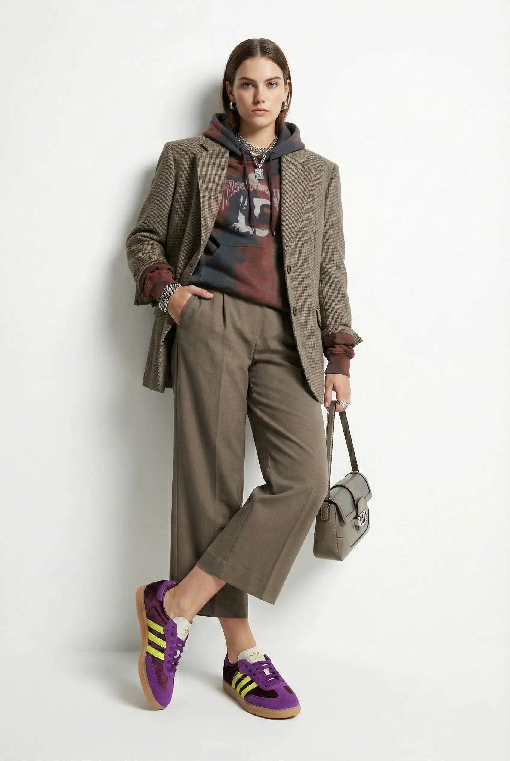 Woman wearing a brown coat, colorful shirt, and purple sneakers against a white background