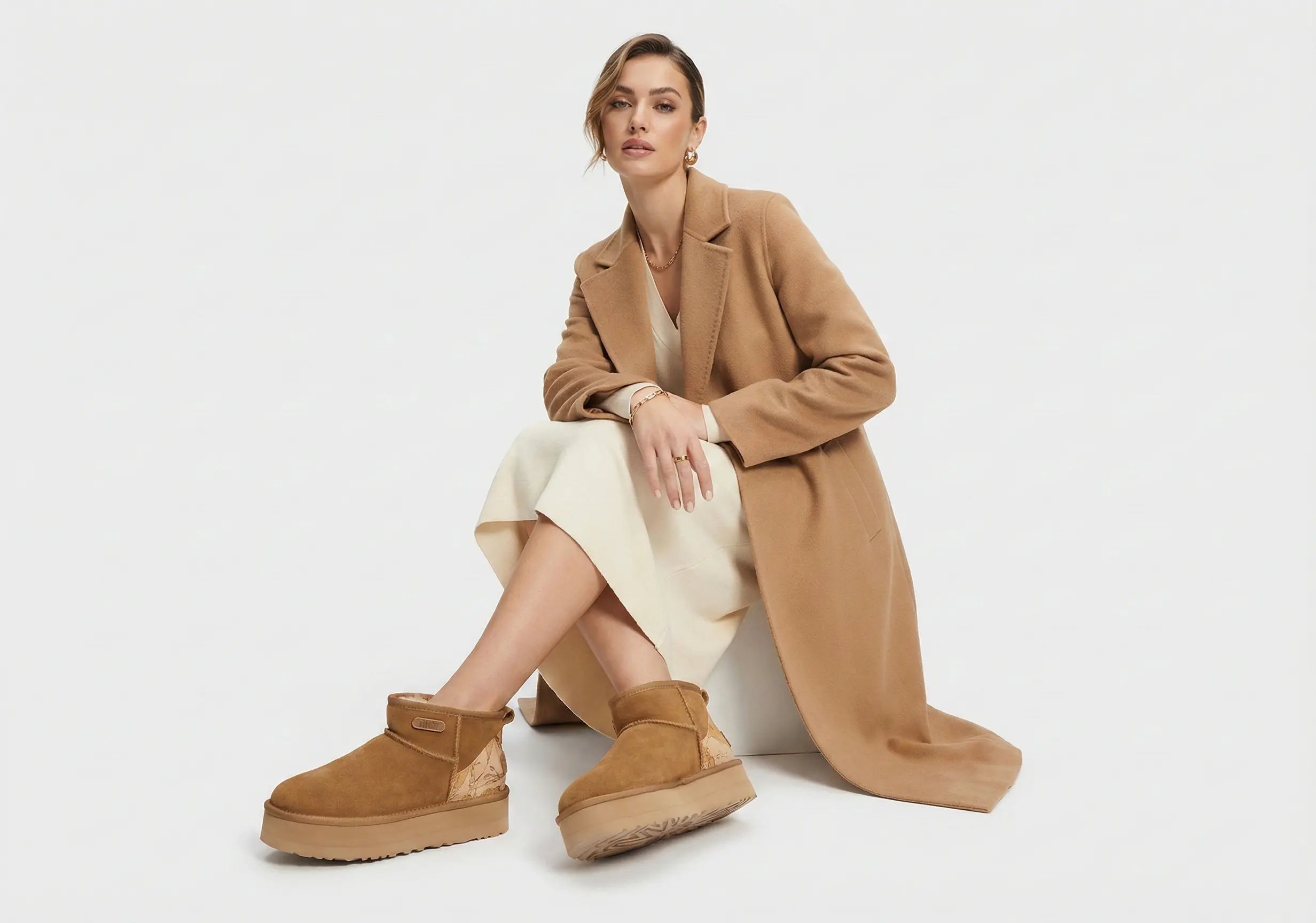 Woman wearing a tan coat and UGG boots on a white background
