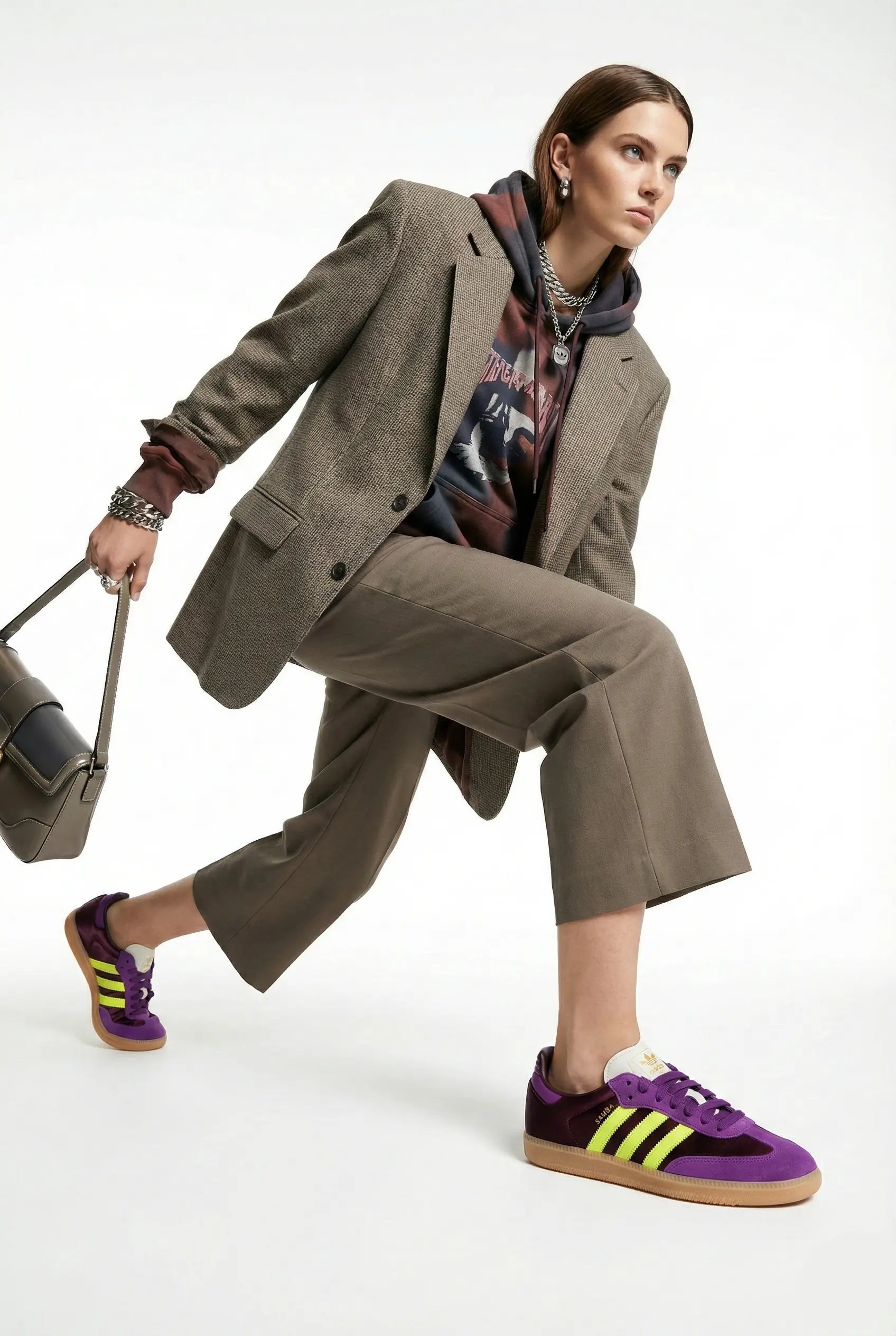 Person wearing a beige suit with a colorful shirt and purple sneakers, holding a bag on a white background